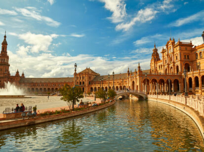 Ein wunderschöner Platz in Sevilla (Spanien). Der Platz wird wird von einem Kanal umringt, der mit 4 Brücken überquerbar ist. Die wunderschönen Gebäude um den Platz herum sind mit Klinkern, Marmor und Keramiken versehen. Inmitten des Platzes befindet sich ein großer Springbrunnen, der alles lebendiger wirken lässt.