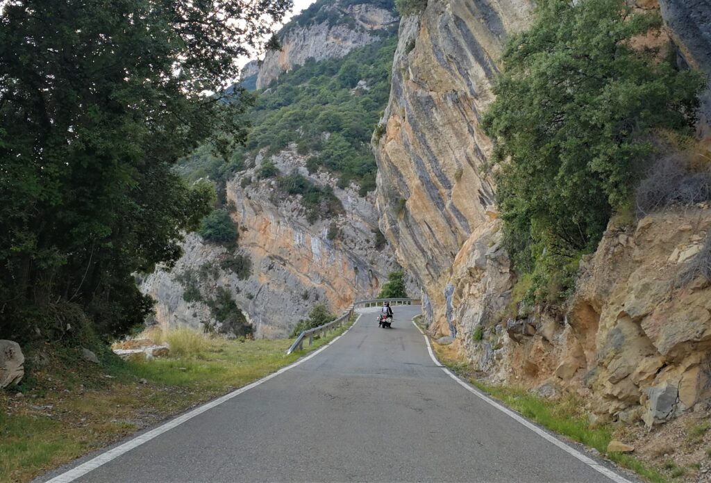 Eine wunderschöne Kulisse inmitten einer Berglandschaft, die auf einer Straße von einem Motorradfahrer und seiner Sozia in den Pyranäen befahren wird.